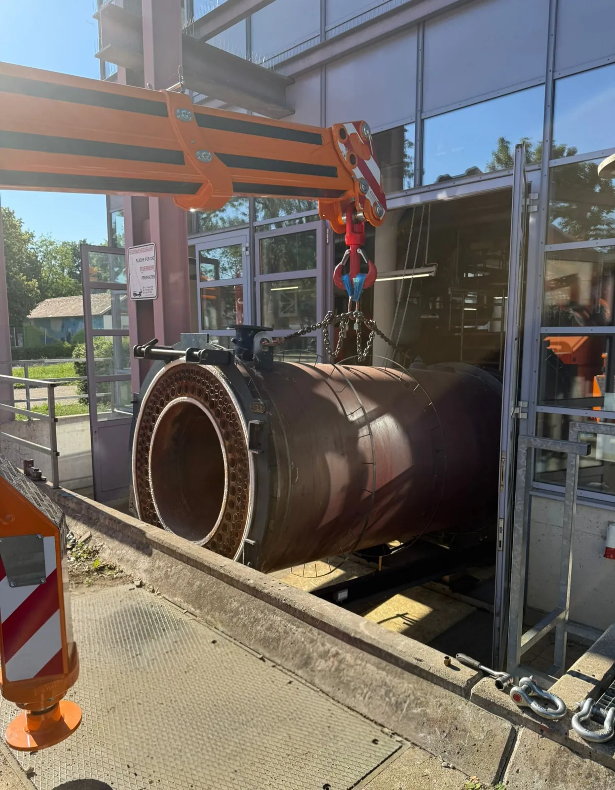 Kessel wird bei engen Platzverhältnissen unter einer Stahlkonstruktion durch die Toröffnung aus dem Gebäude gehoben